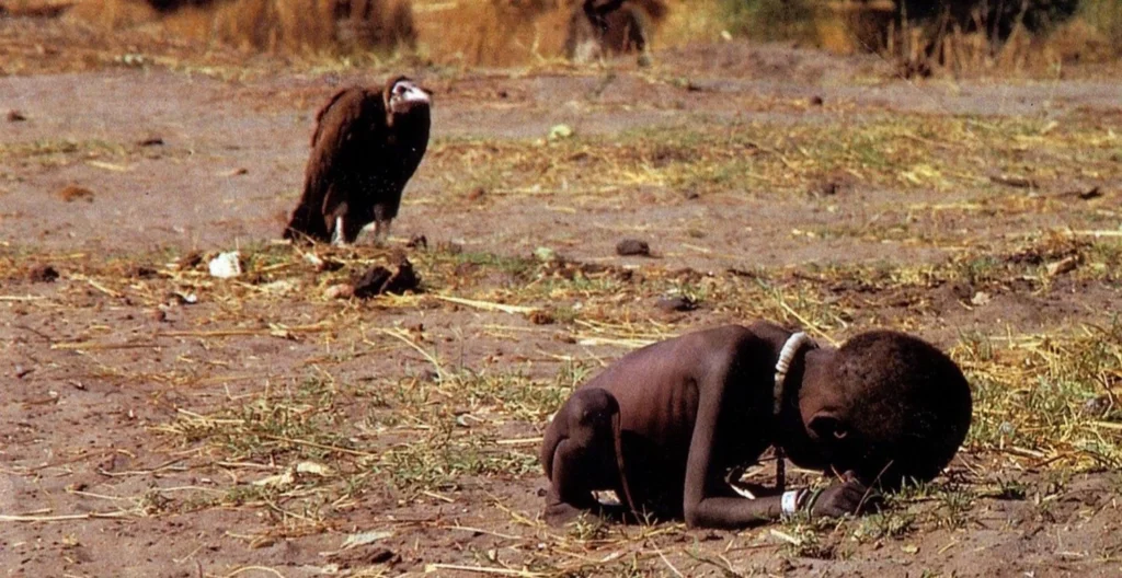 Foto "o abutre e a menina", de Kervin Carter. Uma menina negra de 3 anos aproximadamente está agachada, muito magra, enquanto um urubu a observa.