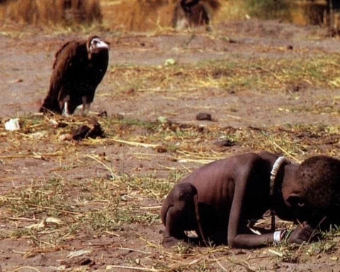 Foto "o abutre e a menina", de Kervin Carter. Uma menina negra de 3 anos aproximadamente está agachada, muito magra, enquanto um urubu a observa.