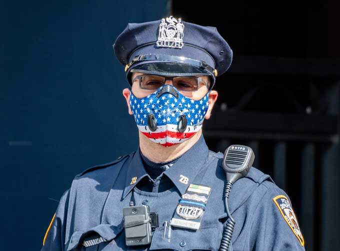 Policial usa máscara de proteção com estampa da bandeira americana no bairro do Brooklyn, em Nova York.