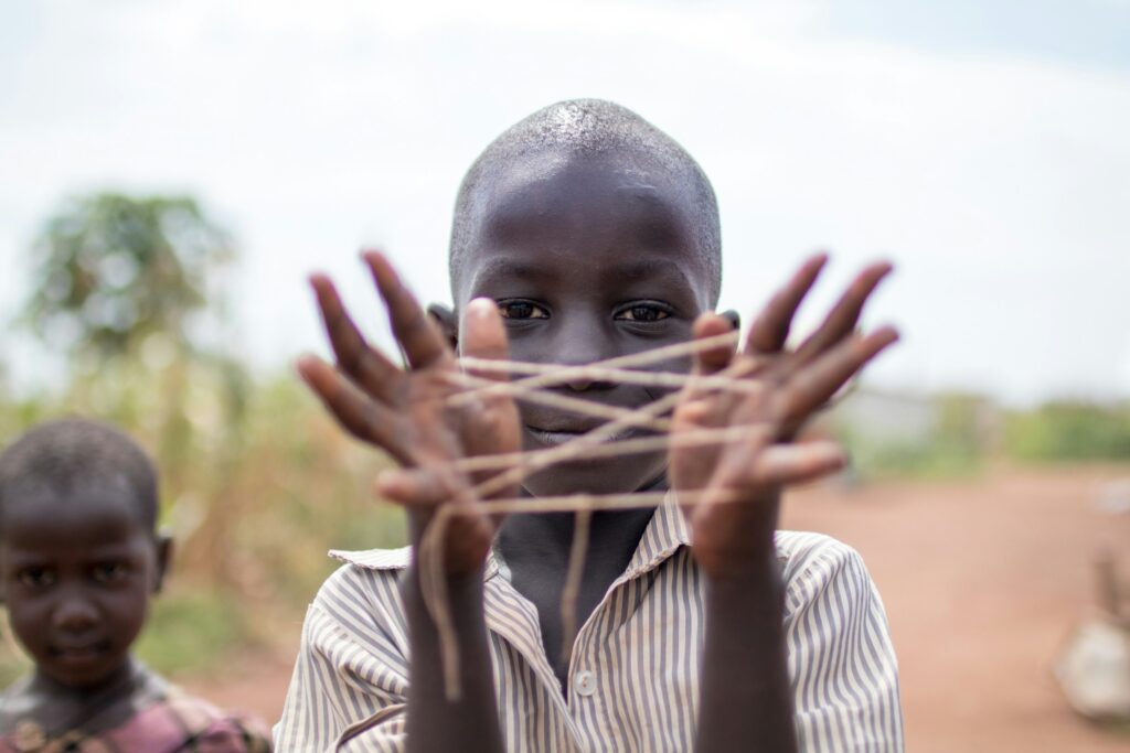 Menino negro brinca com barbantes em forma de labirinto nas mãos, enquanto olha para a câmera. Uma boa representação dos Contos africanos. 