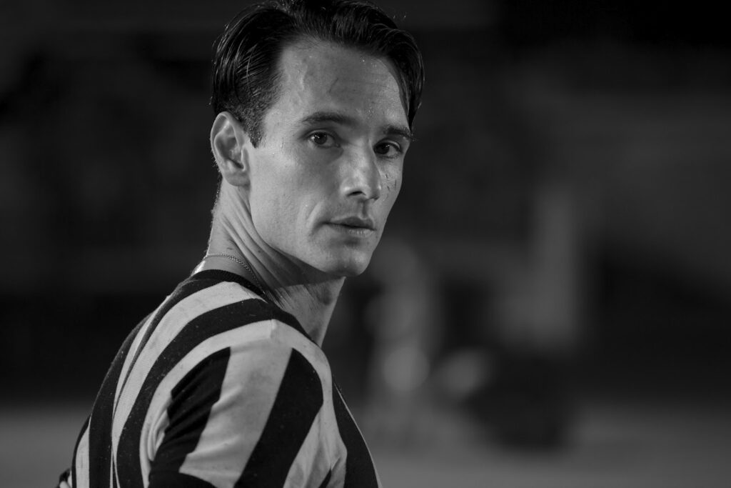 Rodrigo Santoro interpreta Heleno. Ele está com a camisa do Botafogo em fotografia preto e branca, olhando para a câmera em um estádio de futebol.