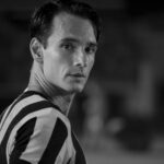 Rodrigo Santoro interpreta Heleno. Ele está com a camisa do Botafogo em fotografia preto e branca, olhando para a câmera em um estádio de futebol.