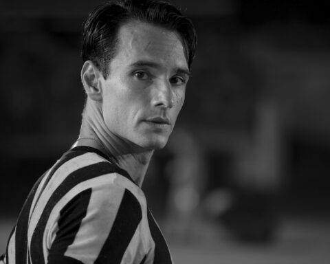 Rodrigo Santoro interpreta Heleno. Ele está com a camisa do Botafogo em fotografia preto e branca, olhando para a câmera em um estádio de futebol.