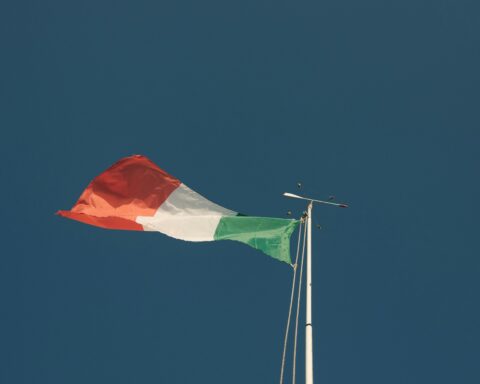 Bandeira italiana tremula contra um céu azul. A foto simboliza a disputa nos tribunais quanto ao massacre nazista de 1943.