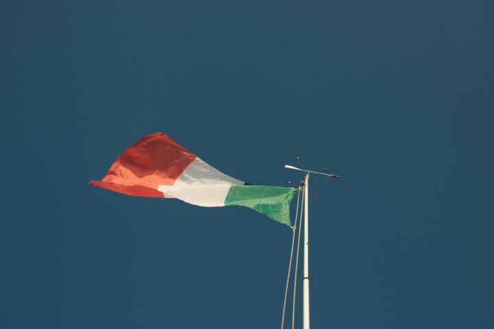 Bandeira italiana tremula contra um céu azul. A foto simboliza a disputa nos tribunais quanto ao massacre nazista de 1943.