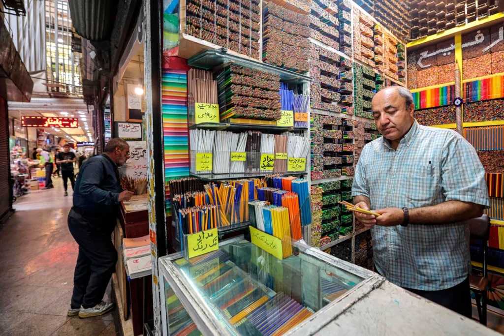 Rafi aparecen dentro de sua colorida loja de lápis de cor, que é pequena, com alguns lápis nas mãos.