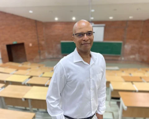 Professor Marcos Aurélio de branco em uma sala de aula. O professor é um homem negro de meia idade.